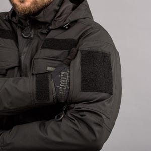 May include: Black tactical jacket with a hood and multiple pockets. The jacket features velcro patches on the sleeves and chest. The gloves have the word "Mechanix" printed on them.