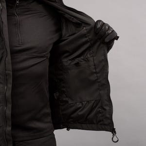 May include: Black jacket with a zippered front and multiple pockets. The interior of the jacket is visible, revealing a dark lining and additional storage compartments. The jacket is designed for outdoor wear.