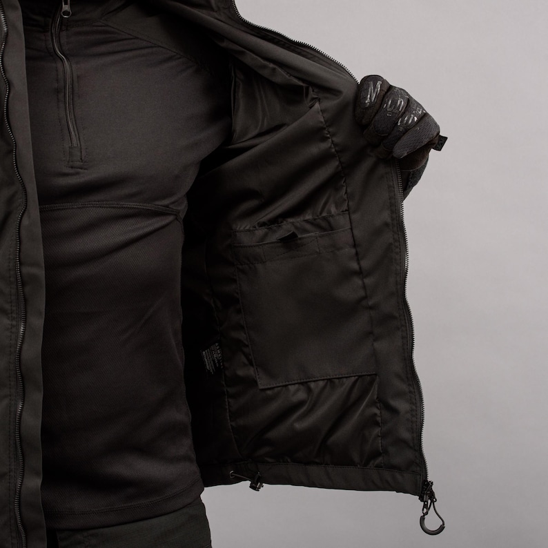 May include: Black jacket with a zippered front and multiple pockets. The interior of the jacket is visible, revealing a dark lining and additional storage compartments. The jacket is designed for outdoor wear.