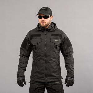May include: Black tactical jacket with multiple pockets, patches, and a hood. The jacket features a front zipper closure, long sleeves, and is worn with a black cap, sunglasses, and gloves. The overall style suggests a military or outdoor theme.