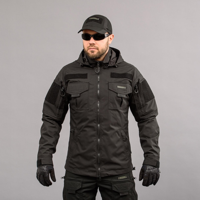 May include: Black tactical jacket with multiple pockets, patches, and a hood. The jacket features a front zipper closure, long sleeves, and is worn with a black cap, sunglasses, and gloves. The overall style suggests a military or outdoor theme.