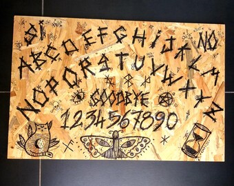 May include: A wooden Ouija board with black lettering and symbols. The board includes the alphabet, numbers 1-9 and 0, and the words "goodbye" and "yes". There is a black cat, butterfly, and hourglass illustration on the board.