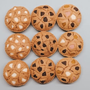 May include: Nine felt cookies in various designs, including chocolate chip, peanut butter, and oatmeal raisin. The cookies are arranged in a 3x3 grid on a light blue background.