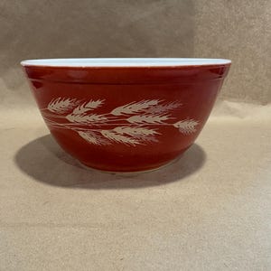 Könnte beinhalten: Eine rote Keramik-Rührschüssel mit weißem Rand und einem Weizenähren-Design. Die Schüssel ist rund und hat eine weite Öffnung, die sich zum Mischen von Zutaten eignet. Das Weizendesign ist cremefarben.