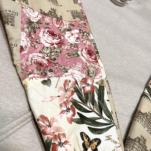 May include: Detail of a beige sweatshirt sleeve with a patchwork design. The patchwork includes floral patterns in pink and cream, a Downton Abbey print, and a butterfly. The sleeve is quilted.