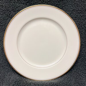 May include: A white ceramic dinner plate with a thin gold rim.