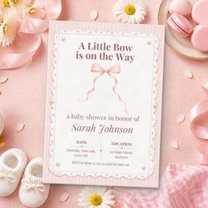 Puede incluir: Una tarjeta de invitaci&oacute;n rectangular para baby shower con borde de rayas rosas y centro blanco con una ilustraci&oacute;n de lazo rosa. El texto dice A Little Bow is on the Way, un baby shower en honor a Sarah Johnson, con fecha, lugar y detalles de RSVP.