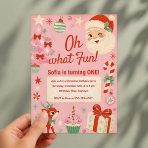 Puede incluir: Una tarjeta de invitaci&oacute;n de cumplea&ntilde;os rectangular de color rosa con un Santa Claus que gui&ntilde;a un ojo, un &aacute;rbol de Navidad decorado, un reno, un cupcake y un regalo. El texto dice: Oh what Fun! Sofia is turning ONE! Join us for a Christmas birthday party.
