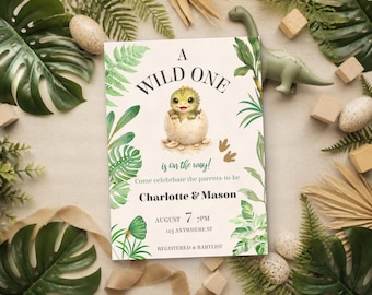 May include: A rectangular invitation card featuring a green baby dinosaur hatching from an egg, surrounded by tropical leaves. The text reads A WILD ONE is on the way! Come celebrate the parents to be Charlotte & Mason AUGUST 7 7PM 123 ANYWHERE ST REGISTERED AT BABYLIST.