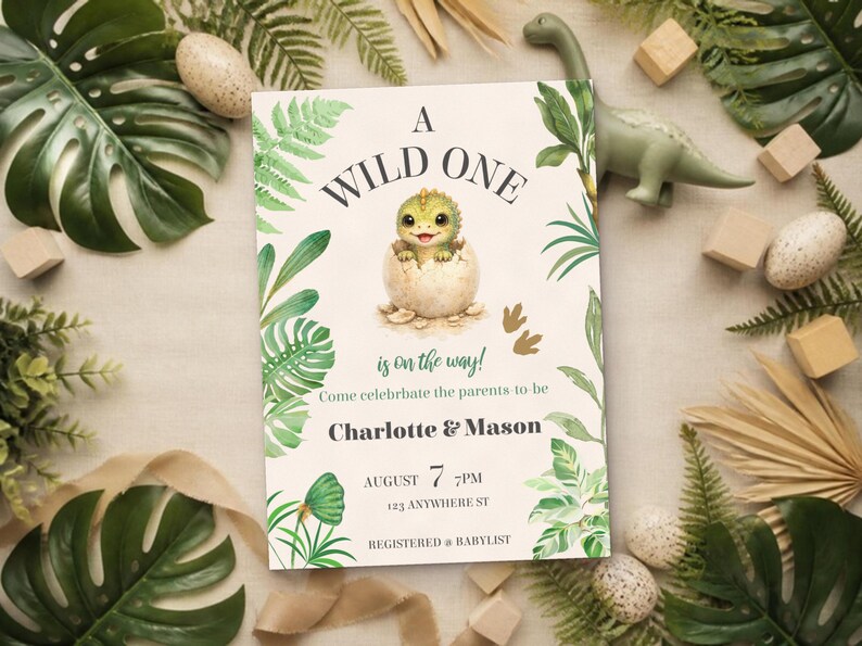 May include: A rectangular invitation card featuring a green baby dinosaur hatching from an egg, surrounded by tropical leaves. The text reads A WILD ONE is on the way! Come celebrate the parents to be Charlotte & Mason AUGUST 7 7PM 123 ANYWHERE ST REGISTERED AT BABYLIST.