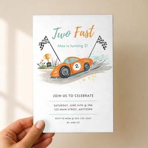 May include: A rectangular birthday invitation card featuring an orange race car with the number 2, two checkered flags, and a gold trophy. The text reads Two Fast, Max is turning 2!, JOIN US TO CELEBRATE, SATURDAY, JUNE 14TH @ 1PM, 123 MAIN STREET, ANYTOWN, RSVP TO MOM @ 555-123-4567 BY JUNE 1ST.