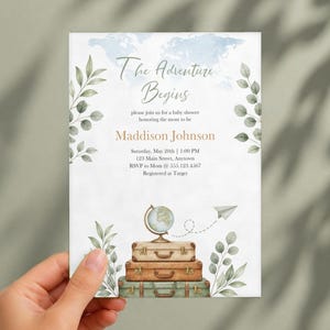 May include: A rectangular baby shower invitation card featuring a watercolor world map background, green leaf illustrations, and a stack of three vintage suitcases topped with a globe. Text reads: The Adventure Begins, Maddison Johnson.