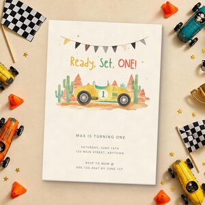 May include: A birthday invitation card featuring a yellow race car with the number one, desert landscape, and bunting. The text reads Ready, Set, ONE! Max is turning one, Saturday, June 14th, 123 Main Street, Anytown, RSVP to Mom at 555.123.4567 by June 1st.