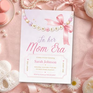Puede incluir: Una tarjeta de invitación rectangular para baby shower con tonos rosas y blancos. En la parte superior muestra un collar de cuentas con el texto MOM ERA y un lazo rosa. El texto de la tarjeta dice In her Mom Era, honrando a Sarah Johnson.