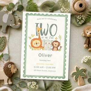 May include: A rectangular invitation card with a scalloped sage green border featuring illustrations of a giraffe, lion, elephant, and monkey. The text reads: Join us to celebrate TWO AT THE ZOO, Oliver, turning two, Saturday, June 14th, 11:00 AM - 2:00 PM, 123 Main Street, Anytown.