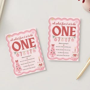 May include: Two rectangular birthday invitations with a scalloped pink border. The text reads "oh what fun it is to be ONE" in red. Graphics include a string of ornaments, a pink Christmas tree, and a cake with a single candle.