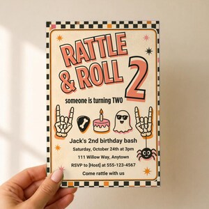 Puede incluir: Una tarjeta de invitaci&oacute;n de cumplea&ntilde;os rectangular con un borde a cuadros negro y naranja. El texto dice RATTLE & ROLL 2, someone is turning TWO, Jack's 2nd birthday bash, Saturday, October 24th at 3pm, 111 Willow Way, Anytown, RSVP to 555-123-4567, Come rattle with us. Los gr&aacute;ficos incluyen manos de esqueleto, una p&uacute;a de guitarra, un pastel, un fantasma y una ara&ntilde;a.