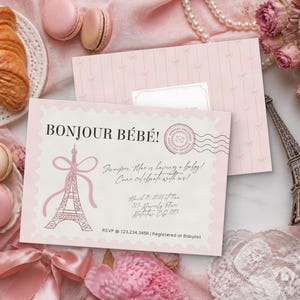 Puede incluir: Una tarjeta de invitación rectangular para baby shower con borde festoneado, que presenta el texto Bonjour Bébé!, una ilustración de la Torre Eiffel rosa con un lazo y detalles del evento, incluyendo la fecha 10 de marzo de 2026 y RSVP 123.234.3456.