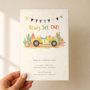 May include: A rectangular birthday invitation card featuring a yellow race car with the number one, desert cacti, and red rock formations. Above the car, a banner hangs with the text Ready, Set, ONE! Below, the text reads MAX IS TURNING ONE, SATURDAY, JUNE 14TH, 123 MAIN STREET, ANYTOWN, RSVP TO MOM @ 555.123.4567 BY JUNE 1ST.