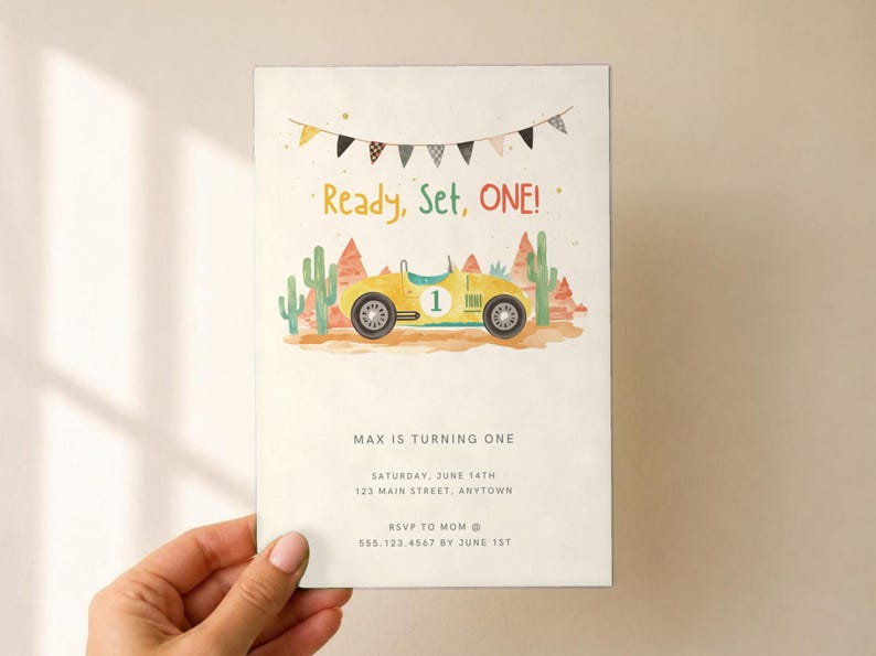 May include: A rectangular birthday invitation card featuring a yellow race car with the number one, desert cacti, and red rock formations. Above the car, a banner hangs with the text Ready, Set, ONE! Below, the text reads MAX IS TURNING ONE, SATURDAY, JUNE 14TH, 123 MAIN STREET, ANYTOWN, RSVP TO MOM @ 555.123.4567 BY JUNE 1ST.