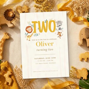 May include: A rectangular birthday invitation card with the text TWO, featuring illustrations of a lion, giraffe, elephant, and monkey. The card includes the name Oliver, the date Saturday, June 14th, and event details, surrounded by wooden animal figures.
