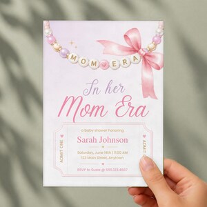 Puede incluir: Una tarjeta de invitaci&oacute;n rectangular para baby shower con un collar de cuentas rosas y blancas y un lazo de cinta rosa. El texto dice In her Mom Era, a baby shower honoring Sarah Johnson, Saturday, June 14th, 11:00 AM, 123 Main Street, Anytown.