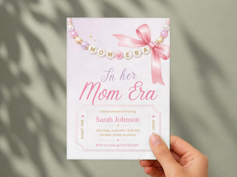 Puede incluir: Una tarjeta de invitaci&oacute;n rectangular para baby shower con un collar de cuentas rosas y blancas y un lazo de cinta rosa. El texto dice In her Mom Era, a baby shower honoring Sarah Johnson, Saturday, June 14th, 11:00 AM, 123 Main Street, Anytown.