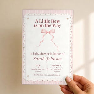 Puede incluir: Una tarjeta de invitaci&oacute;n rectangular para baby shower con borde de rayas rosa claro y encaje blanco. El texto dice A Little Bow is on the Way, con una ilustraci&oacute;n de un lazo rosa, el nombre Sarah Johnson y los detalles del evento.