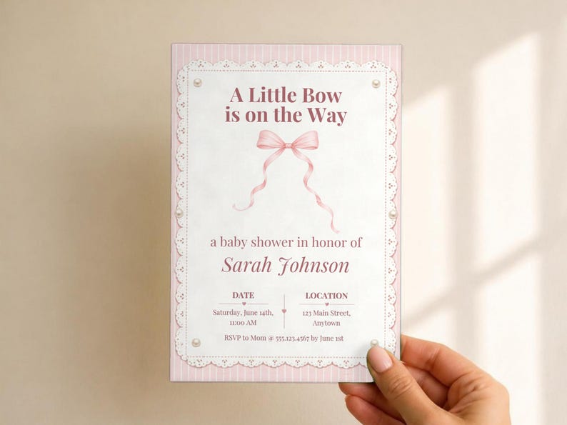 Puede incluir: Una tarjeta de invitaci&oacute;n rectangular para baby shower con borde de rayas rosa claro y encaje blanco. El texto dice A Little Bow is on the Way, con una ilustraci&oacute;n de un lazo rosa, el nombre Sarah Johnson y los detalles del evento.