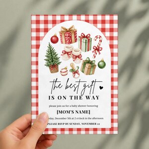 May include: A rectangular baby shower invitation card with a red and white gingham border. The center features watercolor illustrations of Christmas gifts, a tree, a candy cane, and a pacifier, with the text "the best gift IS ON THE WAY".