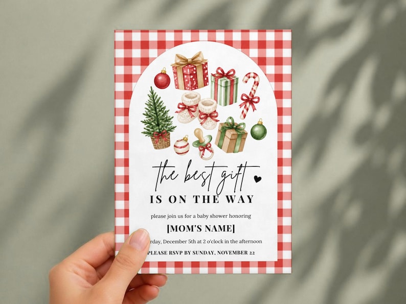 May include: A rectangular baby shower invitation card with a red and white gingham border. The center features watercolor illustrations of Christmas gifts, a tree, a candy cane, and a pacifier, with the text "the best gift IS ON THE WAY".