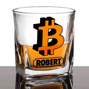 May include: A clear glass rocks glass with a gold liquid inside. The glass has a black and orange Bitcoin symbol with the name "ROBERT" printed on it.