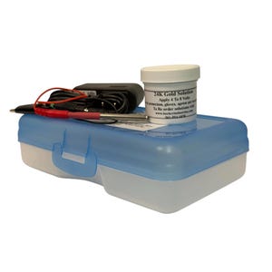 May include: A 24K gold solution kit featuring a white plastic jar with black text, a black power adapter with a red and black probe, and a rectangular storage box with a translucent blue lid and a white base for electroplating applications.