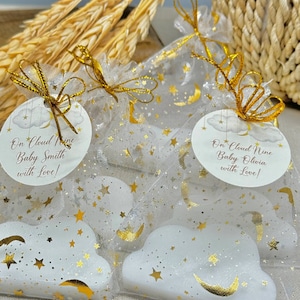 May include: Three white cloud-shaped favors with gold stars and crescent moons, packaged in sheer white bags with gold ribbon and gold stars. The bags have tags that read "On Cloud Nine Baby Smith with Love!" and "On Cloud Nine Baby Olivia with Love!"