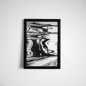May include: Black and white abstract art print in a black frame. The artwork features swirling, liquid-like patterns, creating a dynamic and textured visual effect. The contrast between the black and white elements gives the piece a modern and minimalist aesthetic.