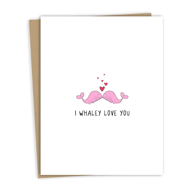 May include: A greeting card with two pink whales kissing with red hearts above them. The text on the card reads "I whaley love you."