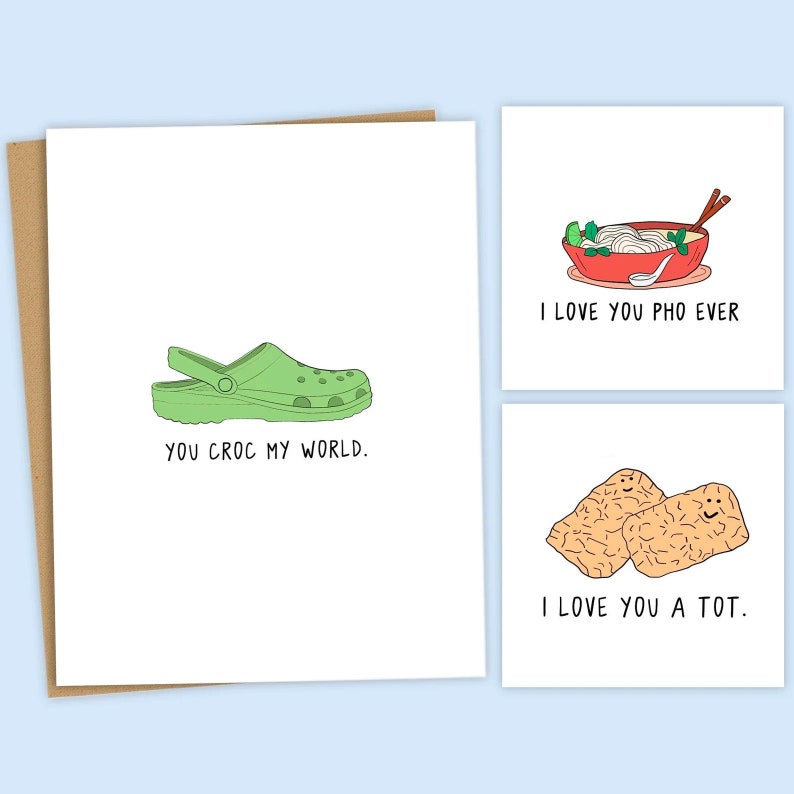 May include: Three greeting cards with funny puns and illustrations. The first card features a green clog with the text "You croc my world." The second card features a bowl of pho with the text "I love you pho ever." The third card features two smiling tater tots with the text "I love you a tot."