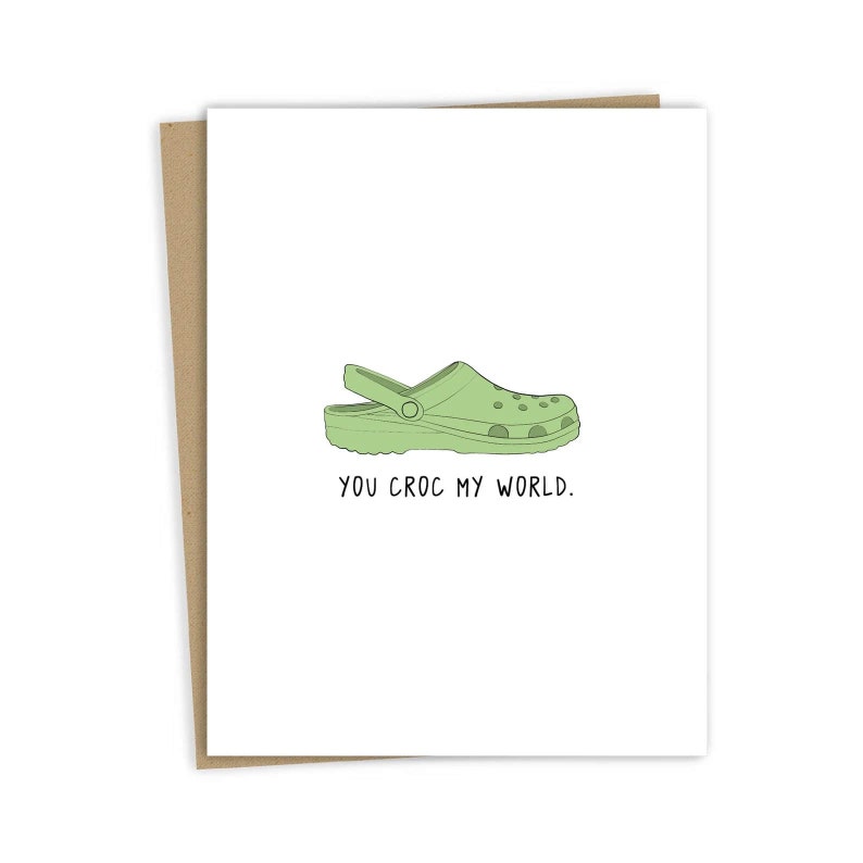 May include: A green and white illustrated card with a green croc shoe and the text "You croc my world."
