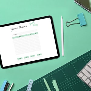 May include: A tablet computer with a blank fitness planner on the screen. The tablet is on a green surface with a keyboard, pencils, a ruler, a stapler, and a binder clip.