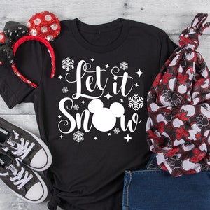 May include: Black t-shirt with a white Mickey Mouse head and the text "Let it Snow" in a white cursive font. The shirt is surrounded by white snowflakes and stars.