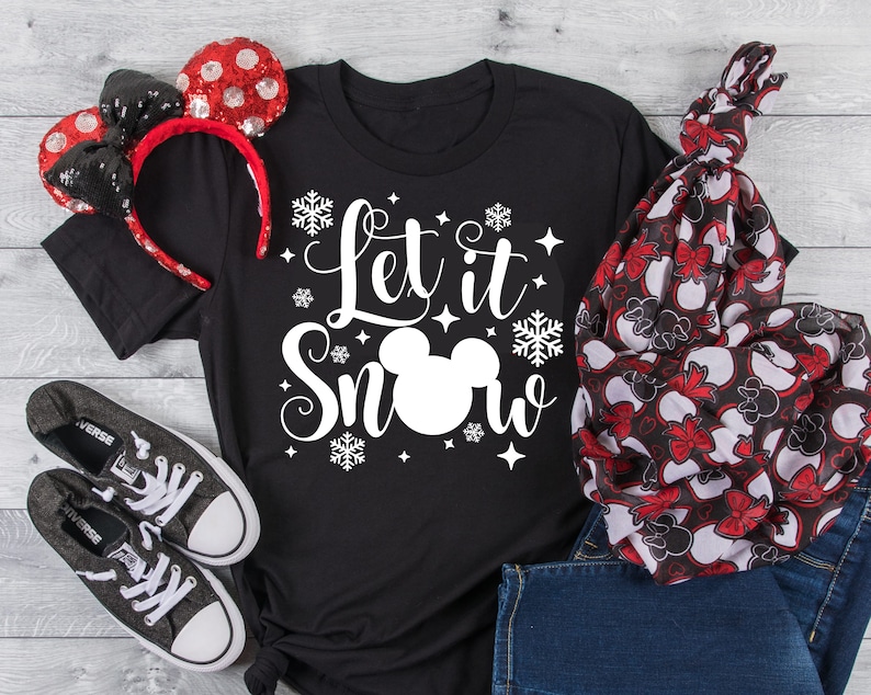 May include: Black t-shirt with a white Mickey Mouse head and the text "Let it Snow" in a white cursive font. The shirt is surrounded by white snowflakes and stars.