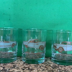 May include: Set of five clear glass tumblers with gold trim and a vintage car design. Each tumbler features a different car model and year, including a 1951 Ford.