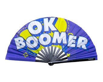 May include: A purple folding fan with the words "OK BOOMER" in large white letters. The fan has a black handle and a design of yellow and blue shapes. The fan is open and displayed against a white background.