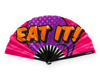 May include: A pink and purple hand fan with black ribs and a white handle. The fan has a comic book style design with the words "EAT IT!" in orange letters.