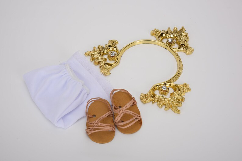 Puede incluir: Un conjunto de ropa de beb&eacute; blanca con una diadema dorada y sandalias marrones. La diadema est&aacute; decorada con pedrer&iacute;a.