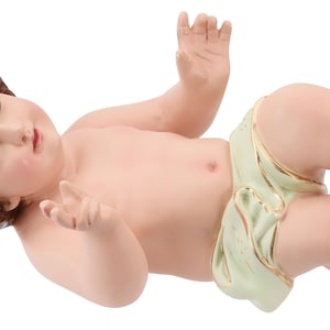 Może przedstawiać: Ceramiczna figurka leżącego na plecach niemowlęcia Jezusa, owiniętego w białą i zieloną pieluchę. Dziecko ma brązowe włosy, niebieskie oczy i spokojny wyraz twarzy.