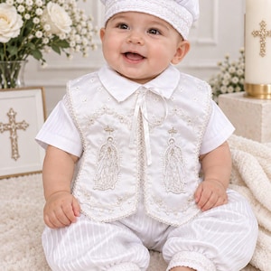 May include: A white baptismal outfit consisting of a short-sleeved shirt with subtle vertical stripes, matching cuffed trousers, and a vest featuring intricate gold and white embroidery of religious figures, paired with a matching white cap.