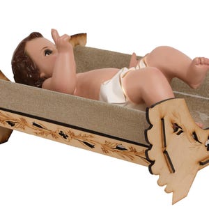 May include: A wooden nativity scene manger with a baby Jesus figurine lying inside. The manger is decorated with a floral design and has a brown fabric lining.