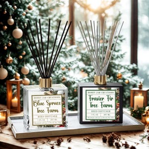 May include: Two reed diffusers with black and silver reeds, labeled "Blue Spruce Tree Farm" and "Frasier Fir Tree Farm." The clear and black square bottles have gold accents and sit on a tray. Each diffuser contains 7 fl oz (207 ml).
