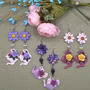 May include: Handmade polymer clay earrings in a variety of floral and teapot designs. The earrings feature purple, white, and yellow flowers, and purple teapots. Each earring has a silver hook and decorative beads.